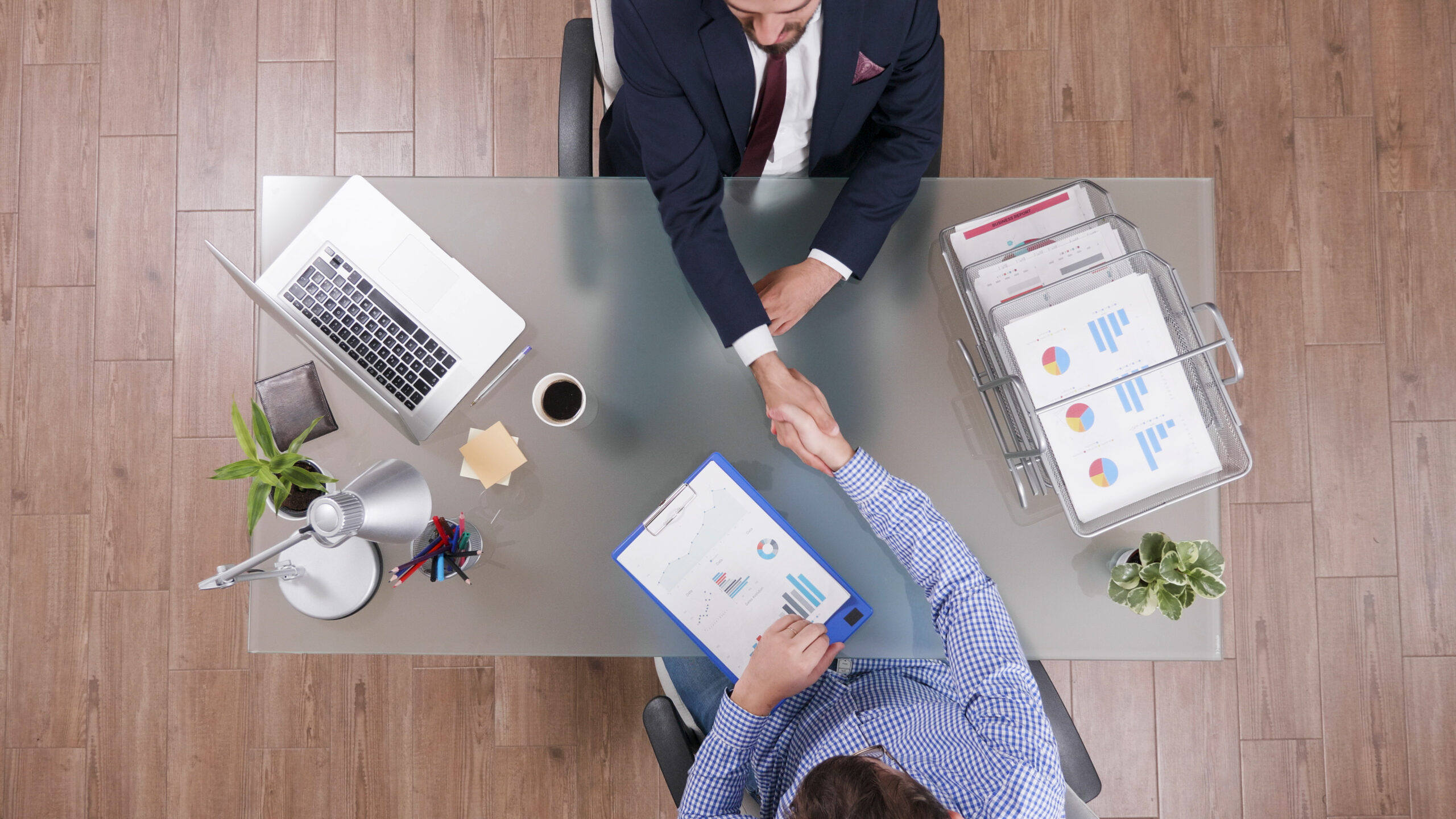top-view-of-businessmen-shaking-hands-during-business-negotiation-in-startup-office-scaled
